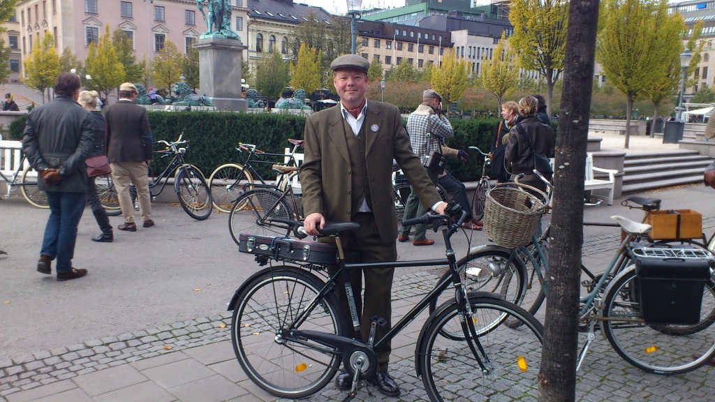 En oerhört stilig man i tweedkostym med cykel och en ukulele i fodral på pakethållaren