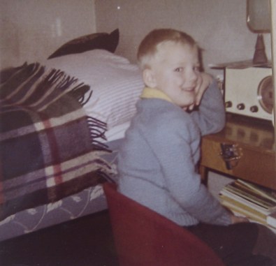 En femårig pojke sitter framför en radio med huvudet stött i handen och armbågen på bordet som radion står på.